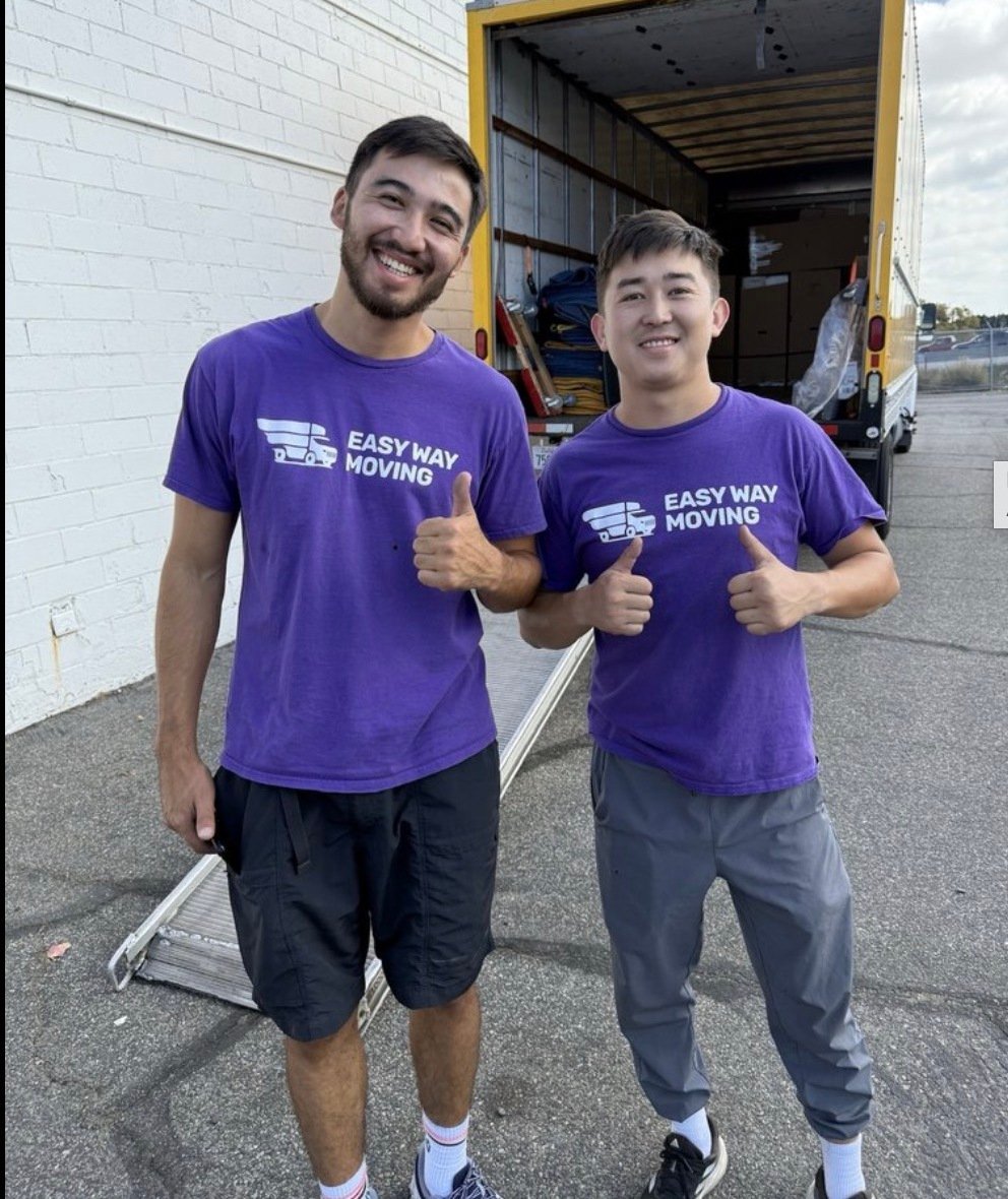 Two Easy Way Moving crew members in branded purple shirts giving a thumbs up in front of their truck